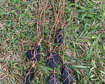 May include: Five black stone pendants wrapped in copper wire on copper chains. The stones are irregular in shape and have a rough texture.