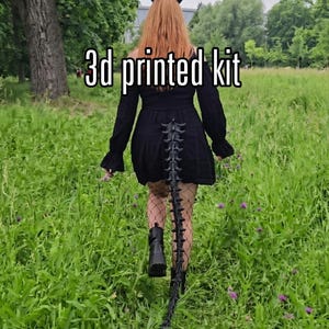 Könnte beinhalten: Ein 3d-gedrucktes Set bestehend aus schwarzen, geschwungenen Hörnern und einem langen, segmentierten, beweglichen Schwanz mit wirbelartiger Struktur. Das Set ist für Kostüme konzipiert und weist eine dunkle, texturierte Oberfläche auf.