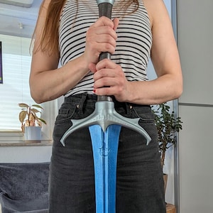 May include: A blue and silver fantasy sword with a detailed hilt and a blue blade. The sword has a decorative design on the blade and a silver crossguard. The hilt is dark brown with a silver and blue pommel.