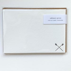 May include: A set of five white flat cards and brown envelopes in clear packaging. A white paper band features the text odinary press FIVE FLAT CARDS + ENVELOPES. A small black graphic of two crossed oars is printed in the bottom right corner.