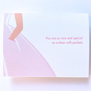 May include: A rectangular greeting card with a white background featuring a stylized illustration of a light pink dress and the text: You are as rare and special as a dress with pockets. The card has a subtle, fine-lined paper texture.