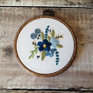 May include: Embroidered hoop art featuring a floral design with blue, green, and yellow flowers on a white background.