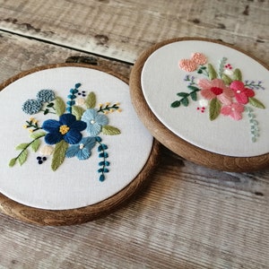 May include: Two embroidery hoops with floral designs. The hoop on the left has blue and green flowers, while the hoop on the right has pink and green flowers.