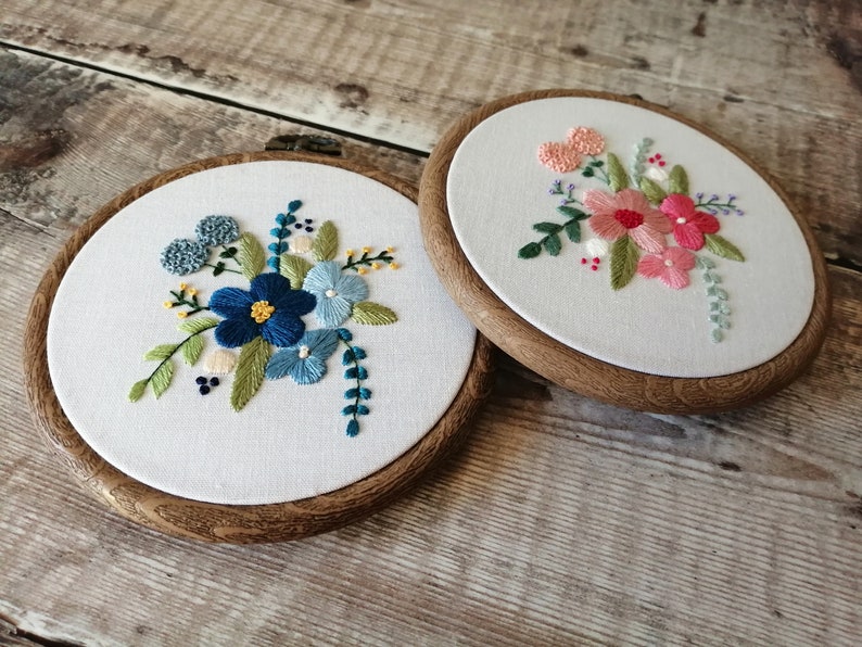 May include: Two embroidery hoops with floral designs. The hoop on the left has blue and green flowers, while the hoop on the right has pink and green flowers.