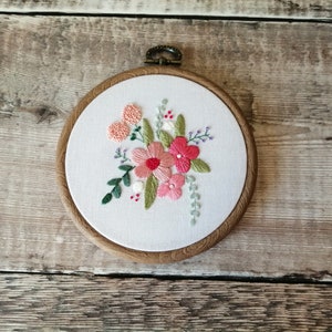 May include: Embroidered floral hoop art with pink and green flowers on a white background. The hoop is made of wood and has a brown finish.