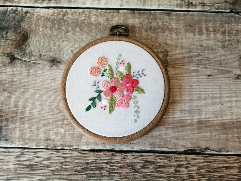 May include: Embroidered floral hoop art with pink and green flowers on a white background. The hoop is made of wood and has a brown finish.