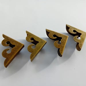 Könnte beinhalten: Vier antike goldene Eckenschutz mit einem dekorativen Design. Die Schutzvorrichtungen sind aus Metall und haben eine patinierte Oberfläche.