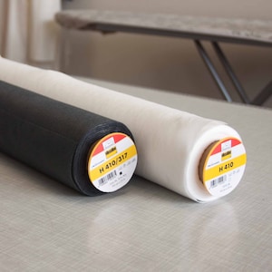 Könnte beinhalten: Zwei Rollen weißer und schwarzer Stoff mit gelben Etiketten. Die Etiketten lauten "Wissene H 410/317 100% PL 300 gr/m2 90 cm x 25 m" und "Wissene H 410 100% PL 300 gr/m2 90 cm x 25 m".