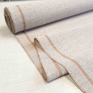 May include: A roll of beige fabric with orange and green stripes. The fabric has a textured surface and a frayed edge.