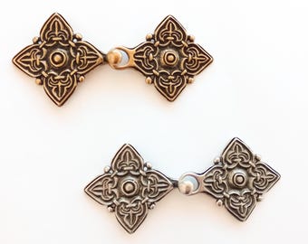 Puede incluir: Dos pares de cierres metálicos decorativos, un par en oro y un par en plata. Cada cierre tiene forma de diamante con intrincados diseños florales.