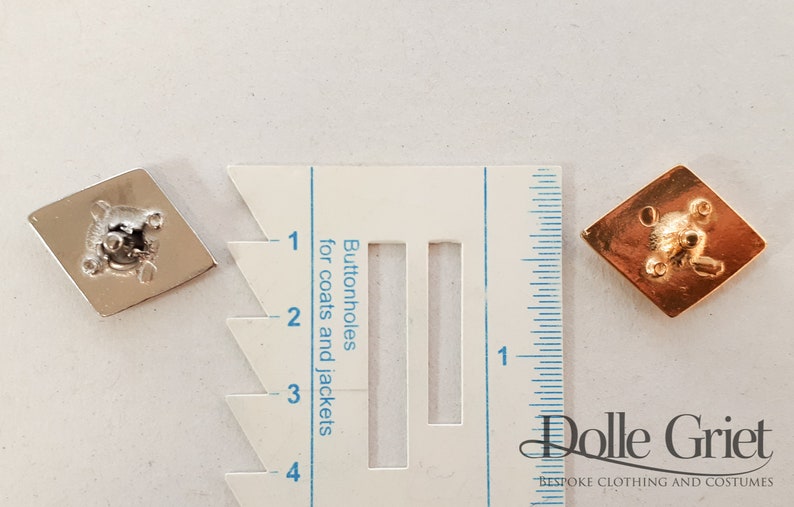 May include: Two diamond-shaped buttonhole cutters, one silver and one gold, are shown next to a ruler marked in inches. The ruler has a section labeled "Buttonholes for coats and jackets".