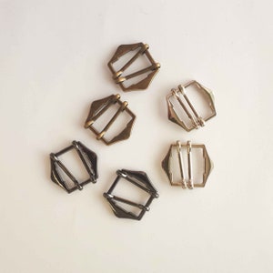 May include: Five metal slider buckles in different finishes. Two are gold, two are silver, and one is black.