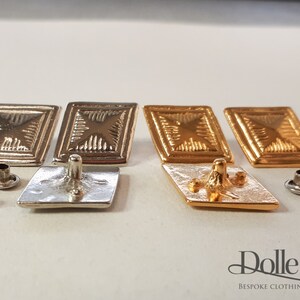 May include: Four square-shaped metal buttons with a raised, textured design. Two buttons are silver, and two buttons are gold. The buttons have a flat back with a small post for sewing.