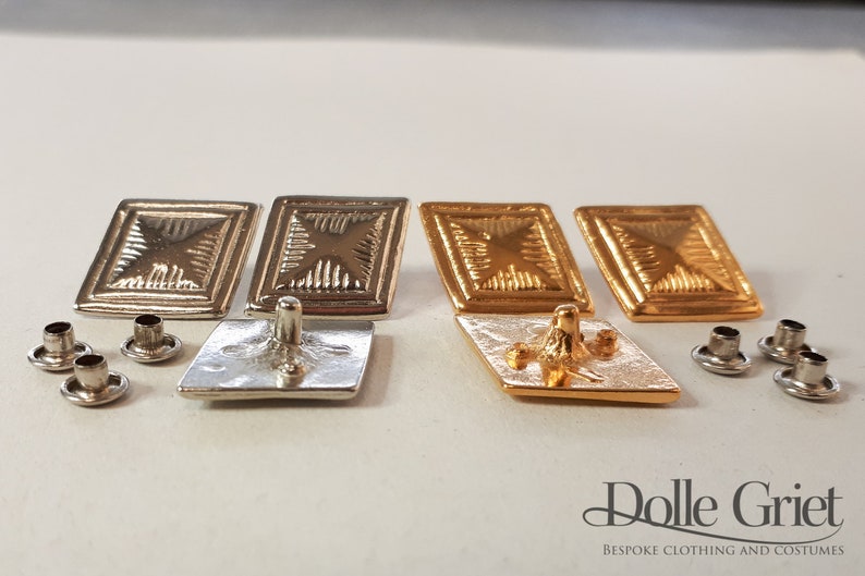 May include: Four square-shaped metal buttons with a raised, textured design. Two buttons are silver, and two buttons are gold. The buttons have a flat back with a small post for sewing.