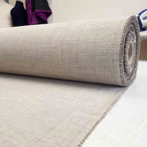 May include: A roll of beige fabric with a textured surface. The fabric is rolled up and the end is visible.