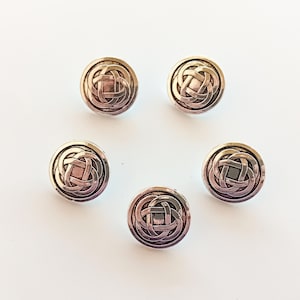 Puede incluir: Cinco botones redondos plateados con un diseño de nudo celta. Los botones tienen un diseño en relieve texturizado y un acabado brillante.