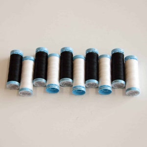 May include: A row of ten spools of thread, five white and five black, with blue plastic caps. The spools are arranged in alternating colours.