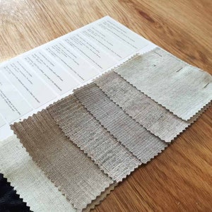 May include: A swatch book of different shades of linen fabric. The swatches are arranged in a row from lightest to darkest. The swatches are all natural linen and have a slightly textured surface.