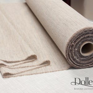 May include: A roll of natural linen fabric, unbleached and with a subtle texture. The fabric is rolled up tightly and has a brown cardboard core. The fabric is on a white surface with the text "Dolle Griet Bespoke Clothing and Costumes" in black.