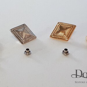 May include: Four decorative metal buttons with a square shape and a raised design. Two buttons are gold, and two are silver. Each button has a small metal post on the back.