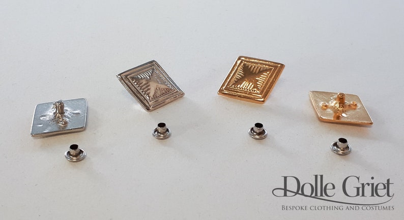 May include: Four decorative metal buttons with a square shape and a raised design. Two buttons are gold, and two are silver. Each button has a small metal post on the back.
