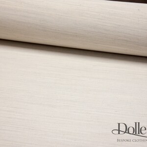 May include: Close-up of a roll of off-white fabric with a subtle woven texture. The fabric is smooth and has a slightly shiny finish. The text "Dolle Griet" is visible at the bottom of the image.