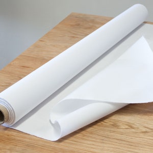 May include: A roll of white canvas fabric on a wooden surface. The canvas is rolled up and partially unrolled, showing the texture of the fabric.