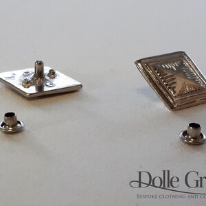 May include: Two silver-toned square buttons with a raised design, and two silver-toned eyelets.  The buttons are for sewing onto clothing or accessories.