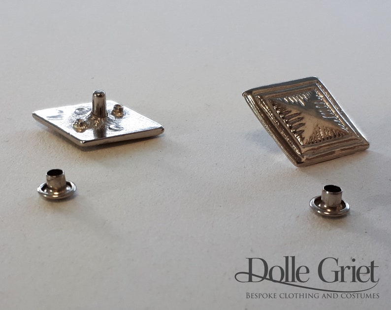 May include: Two silver-toned square buttons with a raised design, and two silver-toned eyelets.  The buttons are for sewing onto clothing or accessories.