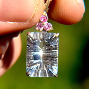 Puede incluir: Un colgante de plata con un gran cristal de cuarzo claro y facetado y tres pequeñas piedras preciosas rosas.