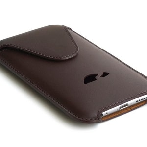 May include: A brown leather phone case with a flap closure. The case has a cutout for the phone's camera and charging port.