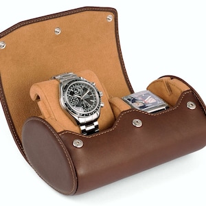 May include: A brown leather watch roll with two compartments for storing watches. The roll is open, revealing a silver watch with a black face and a silver watch with a white face.