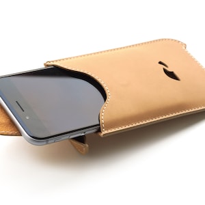 Puede incluir: Una funda de teléfono de cuero marrón claro con un borde cosido y un recorte para la cámara del teléfono. La funda está diseñada para sostener un teléfono inteligente con una pantalla grande.