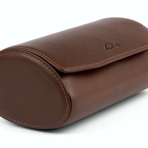 May include: A brown leather watch roll with a stitched seam and a small logo on the top.