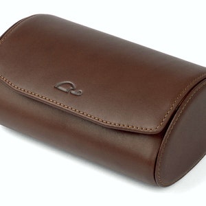 May include: A brown leather watch roll with a stitched seam and a small logo on the top.