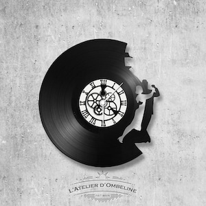May include: A black vinyl record clock with a silhouette of a couple dancing. The clock face features Roman numerals and gears. The text "L'ATELIER D'OMBELINE" and "FAIT-MAIN" is printed below the clock.