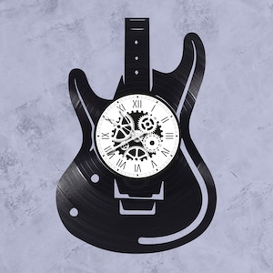 May include: A black vinyl record clock shaped like an electric guitar with a white clock face and roman numeral markings. The clock face has a gear design in the center.