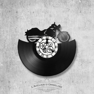 May include: Black vinyl record clock with a silhouette of a motorcycle and gears. The clock face is white with black Roman numerals. The clock is labeled "L'ATELIER D'OMBELINE - FAIT-MAIN".