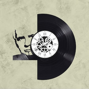 May include: A black vinyl record clock with a white face and Roman numeral hour markers. The clock features a design of gears and cogs in the center.