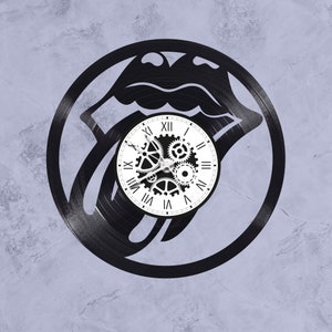 Könnte beinhalten: Schwarze Schallplattenuhr mit einem stilisierten Zungen- und Lippen-Design. Das Zifferblatt der Uhr ist weiß mit schwarzen römischen Ziffern und einem zahnradförmigen Design in der Mitte.