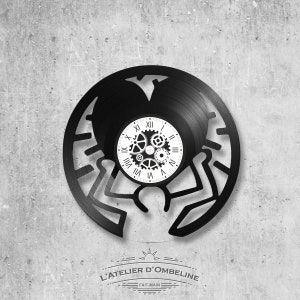 May include: Black vinyl record clock with a silhouette of a person and gears in the center. The clock face has Roman numerals and the text "L'ATELIER D'OMBELINE - FAIT-MAIN".