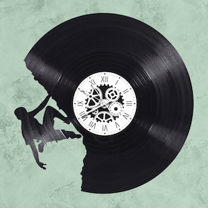 May include: A black vinyl record clock with a white clock face and gears. The record is shaped like a mountain with a silhouette of a person climbing it.
