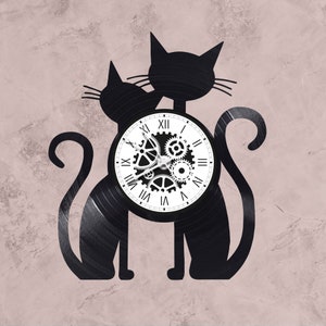 May include: Black vinyl record clock featuring two cats with a clock face in the center. The clock face has Roman numerals and gears.