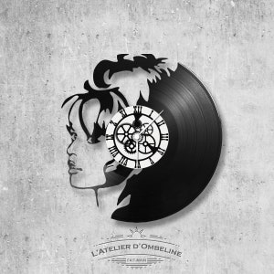 May include: A black vinyl record clock with a silhouette of a person's profile. The clock face is white with black Roman numerals and visible gears. The text "L'ATELIER D'OMBELINE FAIT-MAIN" is at the bottom.