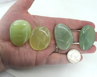 May include: Four smooth, polished green and yellow jade stones, each about the size of a 20 pence coin, are displayed on a hand.