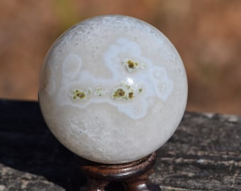 May include: White agate sphere with green inclusions, polished and displayed on a wooden stand.