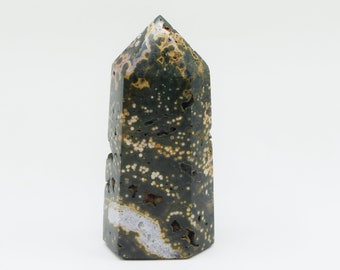 May include: A green, brown, and white speckled stone point, also known as a crystal, with a pointed top and a flat base.