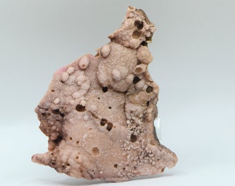 May include: A pink and brown geode with a rough, textured surface. The geode has many small, round holes and a few larger, irregular holes. The geode is about 5 inches tall and 4 inches wide.