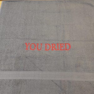 Pu&ograve; includere: Un asciugamano da bagno grigio con la scritta ricamata "YOU DRIED" in rosso. L'asciugamano ha una fascia decorativa vicino al fondo. L'asciugamano &egrave; realizzato in un materiale morbido e assorbente.