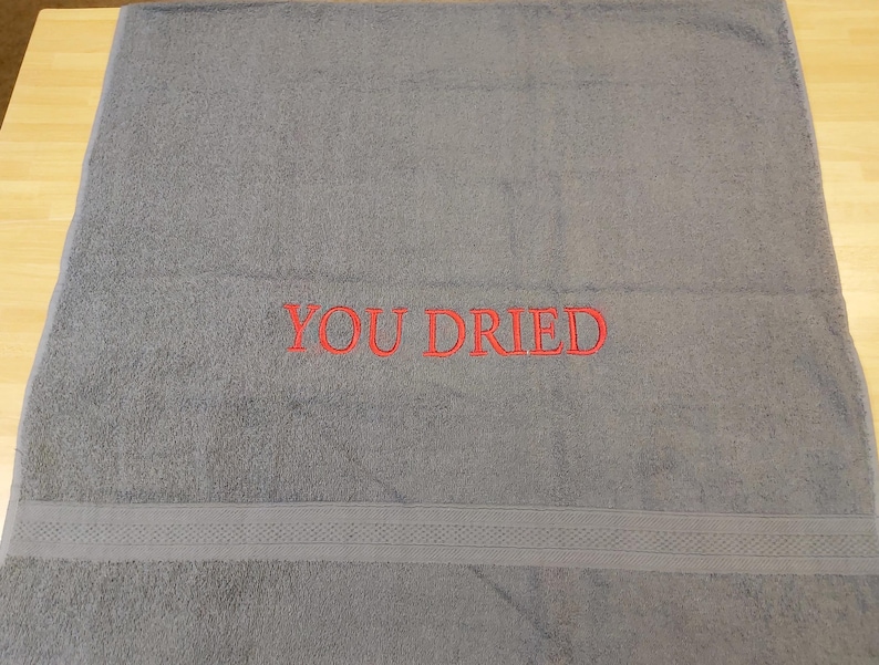 Pu&ograve; includere: Un asciugamano da bagno grigio con la scritta ricamata "YOU DRIED" in rosso. L'asciugamano ha una fascia decorativa vicino al fondo. L'asciugamano &egrave; realizzato in un materiale morbido e assorbente.